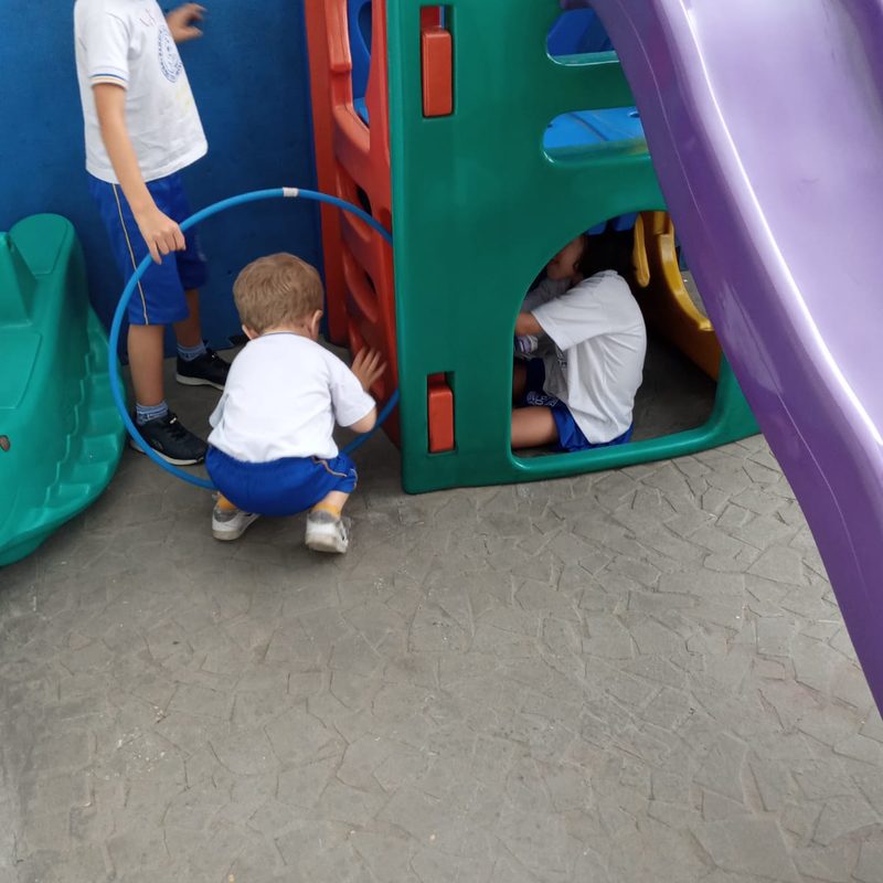 Crianças brincando no escorregador e com bambolê no parquinho